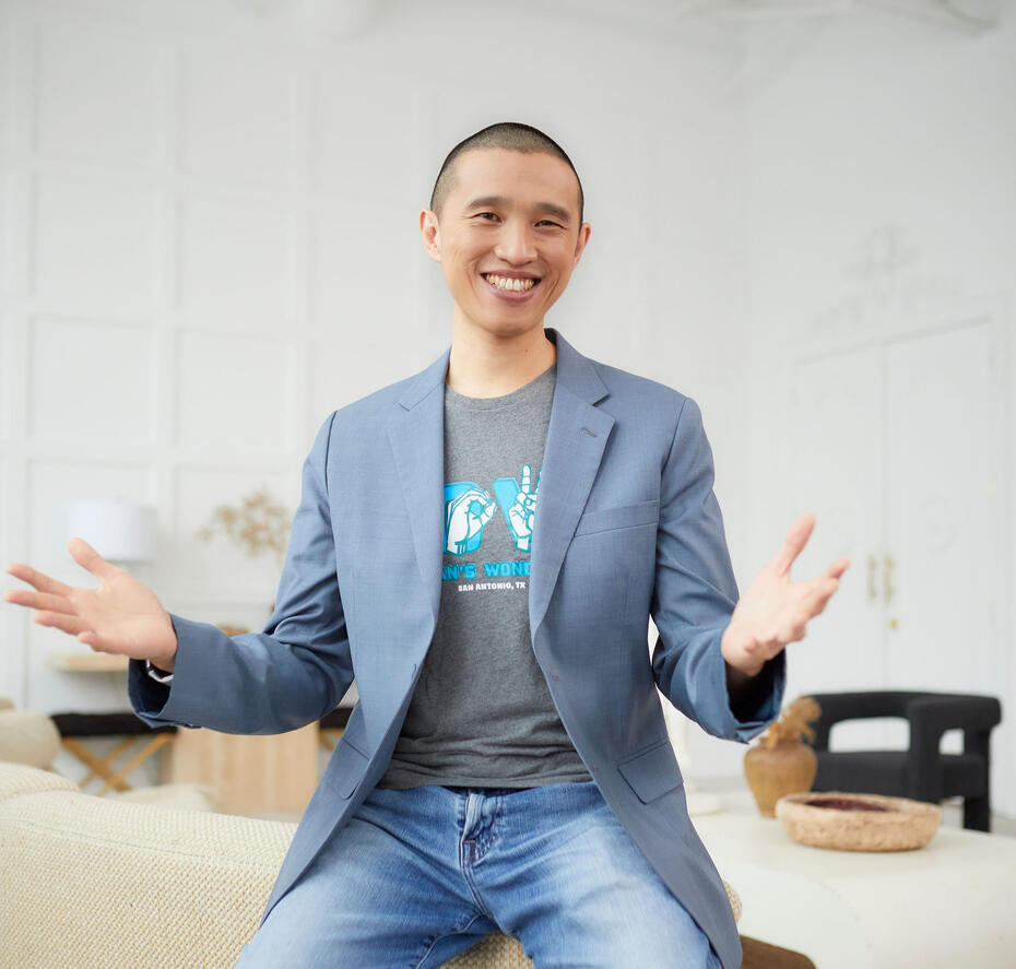 Terrence with blue blazer, grey t-shirt and blue jeans. He's smiling with his arms opened.